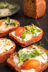 Red beet bread sandwiches with cream cheese, tomatoes and microgreen on black. side view, selective focus.