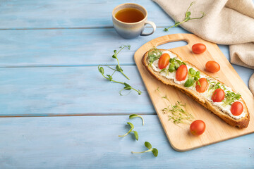 Long white bread sandwich with cream cheese, tomatoes and microgreen on blue. side view.