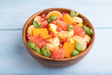 Vegetarian fruit salad of pumpkin, tangerine, pomegranate, microgreen sprouts on blue, side view, close up.
