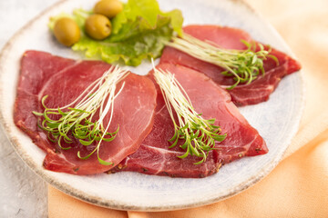 Slices of smoked salted meat with cilantro microgreen on gray. Side view, selective focus.