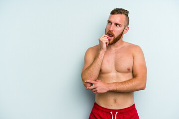 Fototapeta premium Young caucasian man wearing a swimsuit isolated on blue background relaxed thinking about something looking at a copy space.