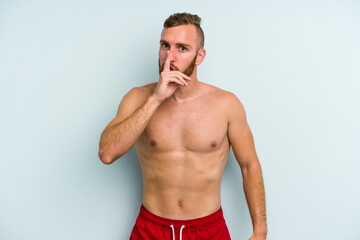 Young caucasian man wearing a swimsuit isolated on blue background keeping a secret or asking for silence.
