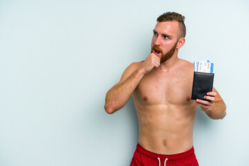 Fototapeta premium Young caucasian man holding a passport isolated on blue background looking sideways with doubtful and skeptical expression.