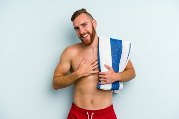Young caucasian man going to the beach holding a towel isolated on blue background laughs out...
