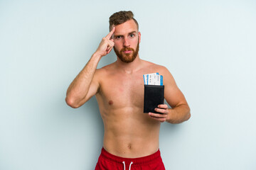 Fototapeta premium Young caucasian man holding a passport isolated on blue background pointing temple with finger, thinking, focused on a task.