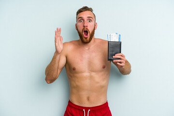 Young caucasian man holding a passport isolated on blue background surprised and shocked.