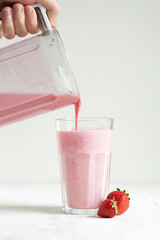 Strawberry smoothie pouring in the glass from blender.