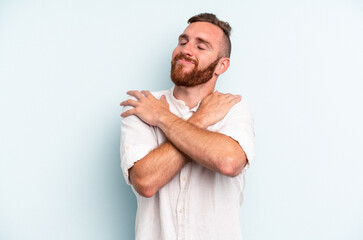 Young caucasian man isolated on blue background hugs, smiling carefree and happy.