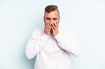Young caucasian man isolated on blue background laughing about something, covering mouth with hands.