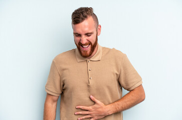 Obraz premium Young caucasian man isolated on blue background touches tummy, smiles gently, eating and satisfaction concept.