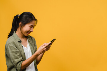 Young Asia lady using phone with positive expression, smiles broadly, dressed in casual clothing feeling happiness and stand isolated on yellow background. Happy adorable glad woman rejoices success.