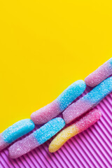 Flat lay of colorful gummy sweets on pink and yellow background.