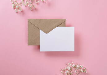 Blank greeting card and envelope with gypsophila on pink background. Blank paper sheet card with mockup copy space. Minimal workplace composition. Flat lay, top view
