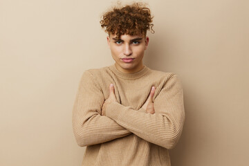 a close horizontal portrait of a handsome, charming man with curly hair standing in a beige sweater on a beige background, hugging himself with his arms