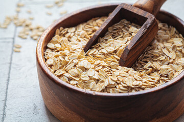 Raw dry oatmeal in wooden bowl, gray background.