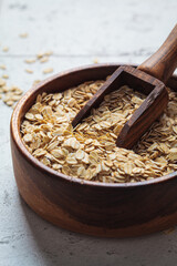 Raw dry oatmeal in wooden bowl, gray background.