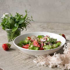 white bowl with salad with radishes, strawberries and pine nuts on the table