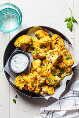 Baked spicy cauliflower with yogurt sauce in black plate. Vegan diet recipe concept.
