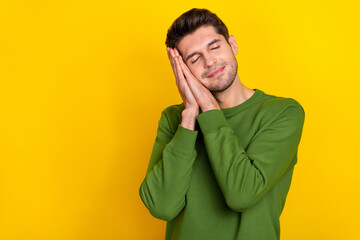 Photo of dreamy tired guy wear green sweater arms cheek sleeping empty space isolated yellow color background