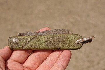 one old green folding knife with a rusty blade lies in the palm of your hand on a gray background