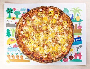 Delicious three cheese pizza with olives and yellow pepper on a colorful table placemat close-up shot 