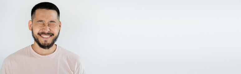 Fototapeta premium portrait of asian man with beard and closed eyes smiling isolated on grey, banner.