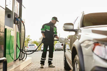 Focused male employee pouring fuel into car tank at gas station