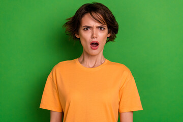 Photo of impressed shocked young woman dressed orange listening bad news open mouth isolated green...