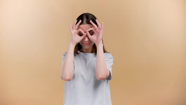 Cheerful young caucasian girl with a smile playing ful at the camera plaine beige background.