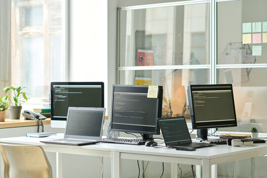 Horizontal image of workplace of IT specialist with codes on screens of computers and laptops on table