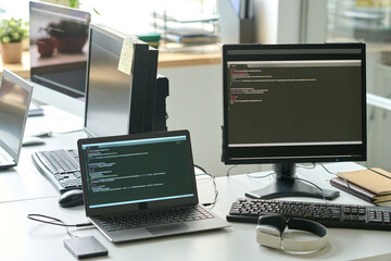 Horizontal image of computer monitor and laptop with software on the screen standing at office desk