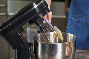 close-up of female hands with a spatula spread the buttercream into the bowl of a culinary mixer. cooking cream for decorating a wedding cake