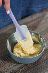 female hands with a spatula stir the buttercream in a plate for decorating a homemade cake