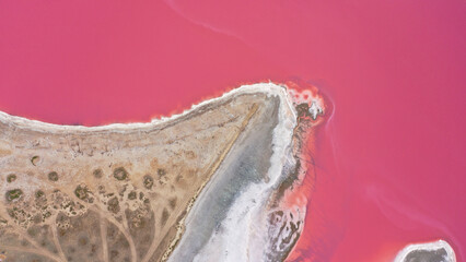 Flying over a pink salt lake. Salt production facilities saline evaporation pond fields in the salty lake. Dunaliella salina impart a red, pink water in mineral lake with dry cristallized salty coast.