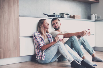 young couple drinking coffee sitting on the kitchen floor