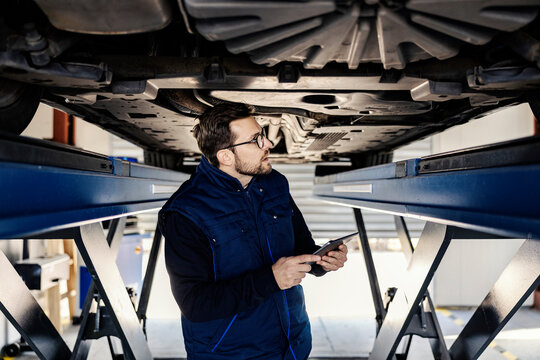 A car service worker looking under the car in garage with tablet in hands. Technical or car service.
