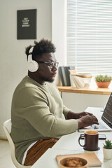 Fototapeta premium African young software developer in wireless headphones concentrating on his online work on laptop