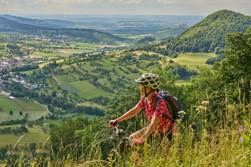 nice senior woman riding her electric mountainbike at a viewpoint on the Swabian Alb above village of Neidlingen, Baden-Württemberg, Germany
