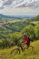 nice senior woman riding her electric mountainbike at a viewpoint on the Swabian Alb above village of Neidlingen, Baden-Württemberg, Germany
