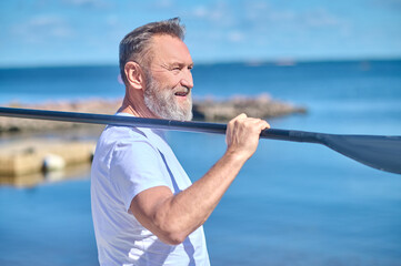 Man with paddle on shoulder standing sideways to camera