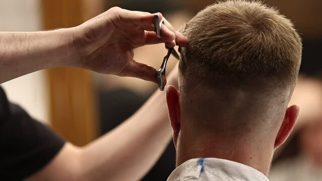 A young male Barber adjusts the hair of a male client. Professional hair care products. Cinematic close-up of a barber giving fade haircut to male client. Slow motion shot of short clipper hairstyle.
