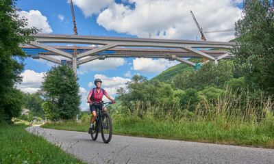 woman on electric mountain bike below the construction site for the new railway trail from Stuttgart to Munich. Combined tunnel and bridge construction in the Fils Valley, Bden-Württemberg, Germany 