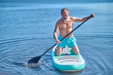 Fototapeta na wymiar Man paddling on surfboard looking at water