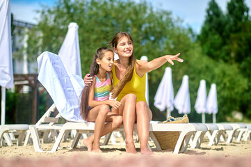 Happy female vacationer sunbathing with her daughter on the sunlounger