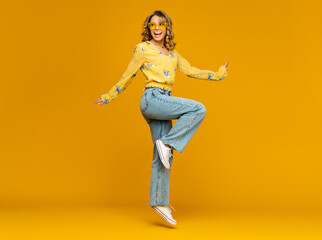 stylish happy smiling blond woman posing in jeans on yellow background