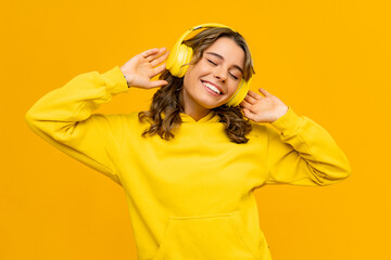 smiling attractive woman listening to music in headphones on yellow background
