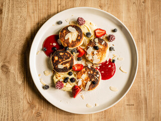 Cheesecakes with English cream, cherry sauce, strawberries, blueberries, currants and almond flakes on a handmade plate.