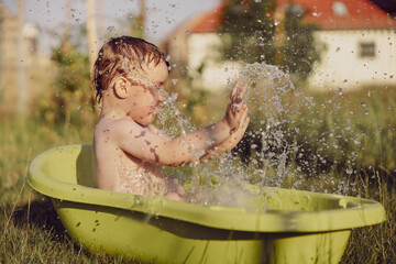 Cute little boy bathing in tub outdoors in garden. Happy child is splashing, playing with water and having fun. Summer season and recreation. Staying cool in the summer heat. Water fun in backyard.