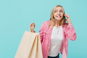 Young woman she 30s in pink shirt white t-shirt holding package bags with purchases after shopping speak on mobile cell phone apologise isolated on plain pastel light blue background studio portrait - obrazy, fototapety, plakaty