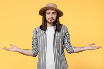 Young man he 20s wears striped grey shirt white t-shirt hat spread hands shrugging shoulders looking puzzled, have no idea isolated on plain yellow color background studio. People lifestyle concept.